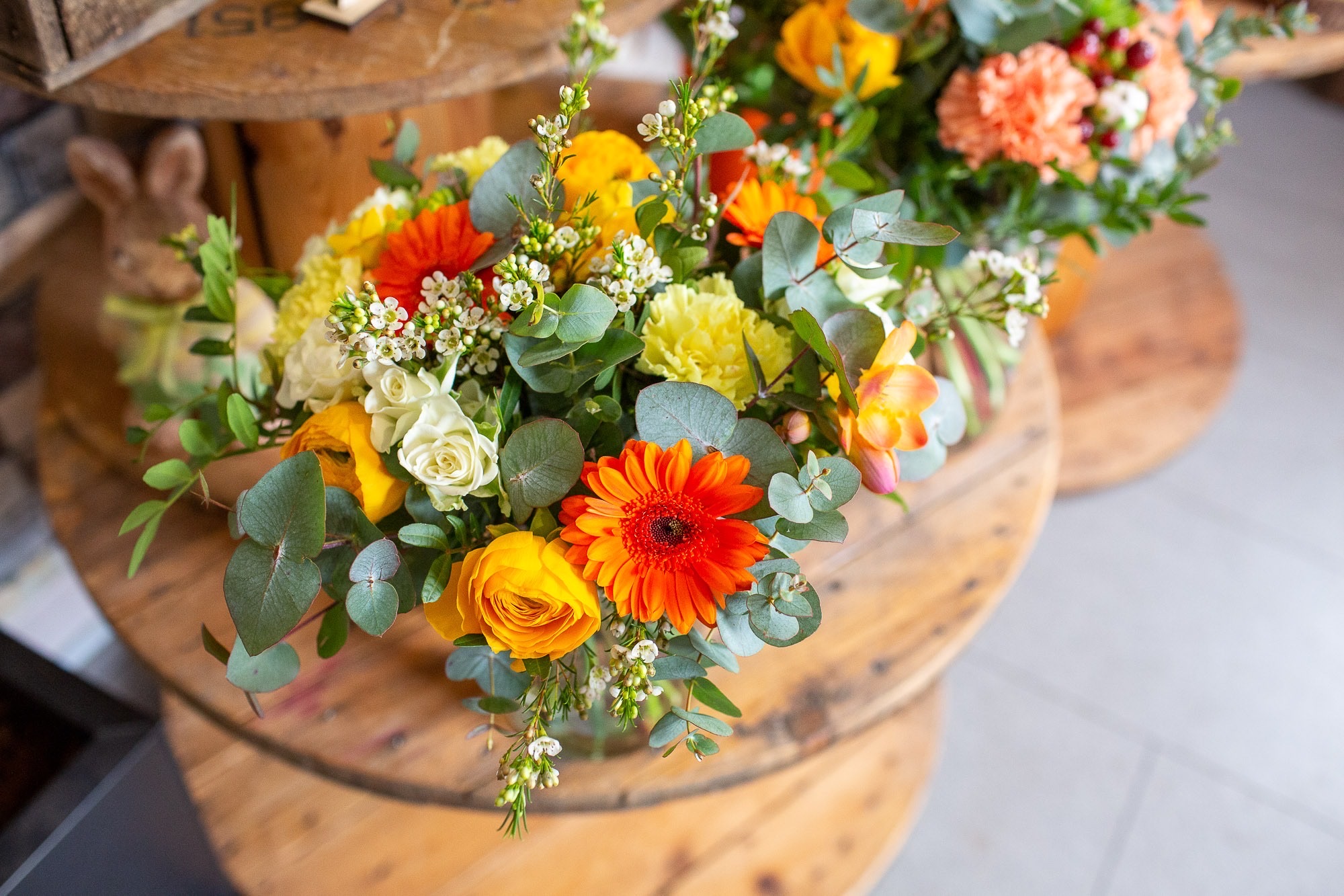 Une création de la boutique : fleurs jaunes et orangées, roses blanches et eucalyptus, sur une table en bois.
